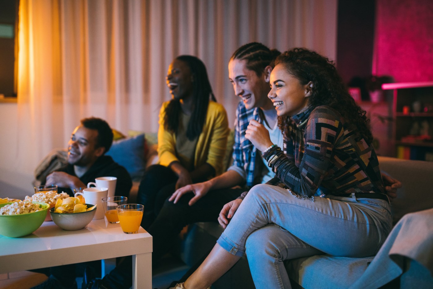 Venner ser på film sammen i stua, ler og nyter snacks og drikke.