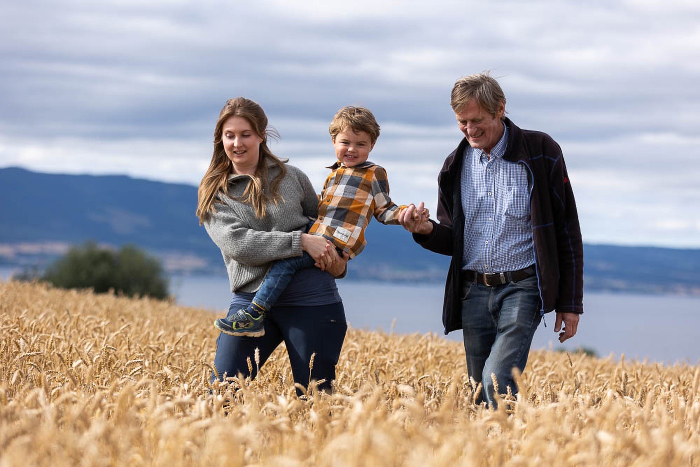 En kvinne bærer en sønn på armen mens hun går over en åker med faren sin