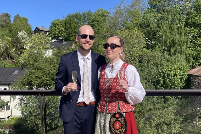 Par i dress og bunad på solfylt balkong.