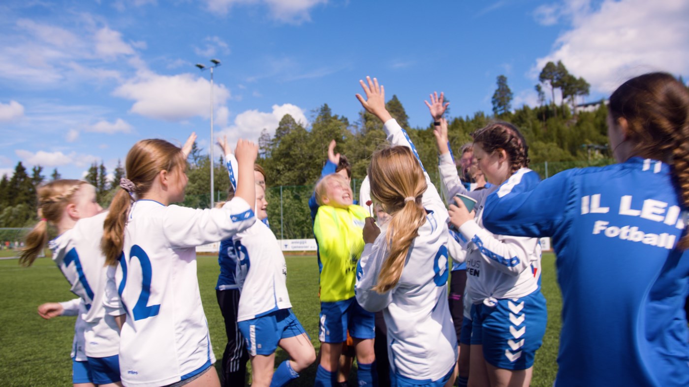 Jenter i fotballdrakt feierer med hender i været.
