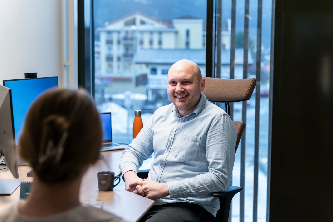 Mann sitter bak en pult og smiler til en kunde.